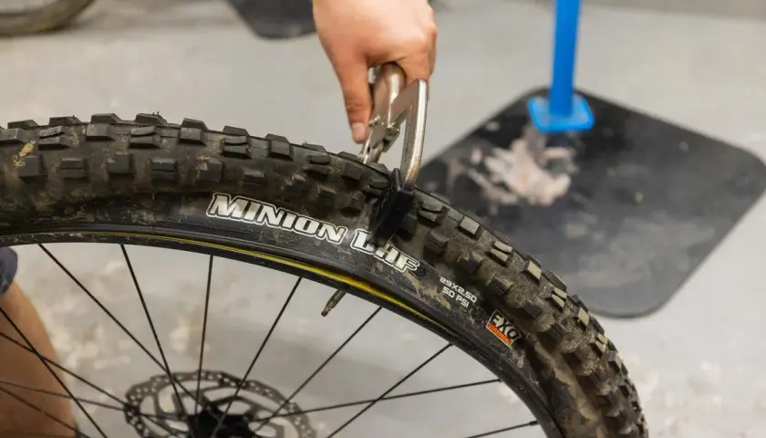Ręka z kombinerkami zaciska oponę rowerową, która jest zwijana, a nie drutowa.