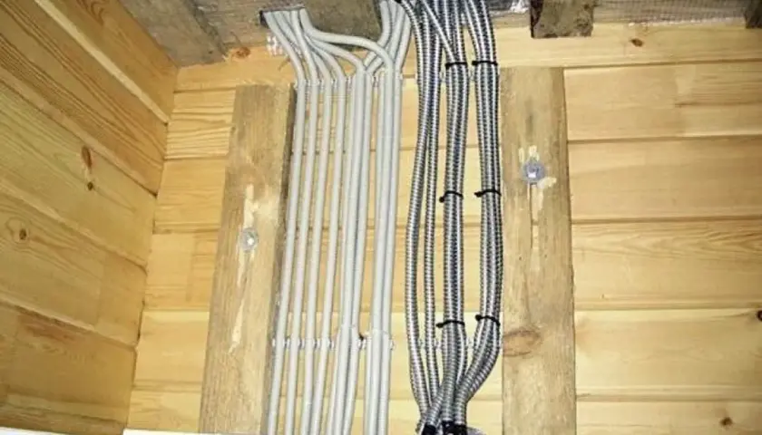 Instalacja elektryczna w domku drewnianym: wiązki kabli w peszlach i metalowych osłonach wychodzą z sufitu.