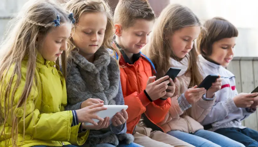 Dzieci skupione na ekranach telefonów i tabletu, szukają najlepszych gier dla 4 latka na telefon.
