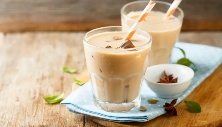 Dwa orzeźwiające **chai latte** z kostkami lodu i słomkami, ozdobione listkami mięty i przyprawami.