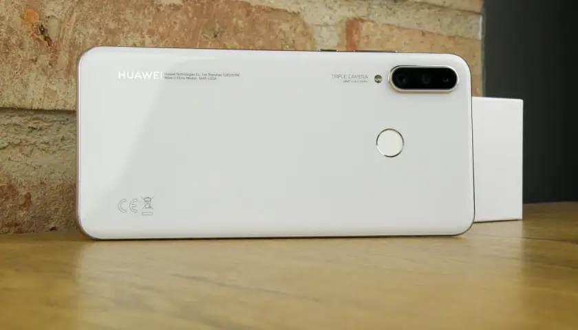 Biały smartfon Huawei MAR-LX1A z potrójnym aparatem i czytnikiem linii papilarnych na drewnianym blacie.