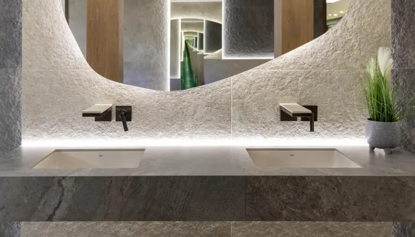 Nowoczesna łazienka z dwoma umywalkami, kamiennymi płytkami i rośliną, idealnie oddająca zasady biophilic design.