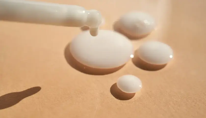 Ein weißes Serum tropft aus einem Applikator auf eine beige Oberfläche. Das ist Panthenol, ein Wirkstoff für Haut und Haar.