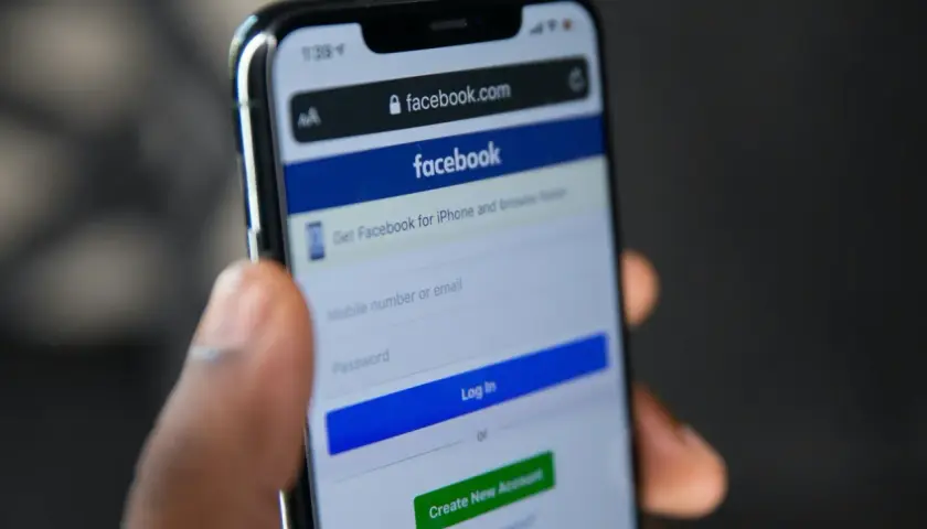 Dłoń trzyma smartfon z ekranem logowania Facebooka. Widoczny formularz do wpisania numeru telefonu/emaila i hasła, przycisk "Log In" oraz opcja "Forgot Password" - pomoc w sytuacji, jak odzyskać konto na FB.