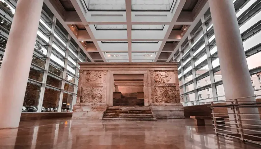 L'Ara Pacis, un altare monumentale con rilievi antichi, si erge maestoso in un moderno spazio espositivo con ampie vetrate.