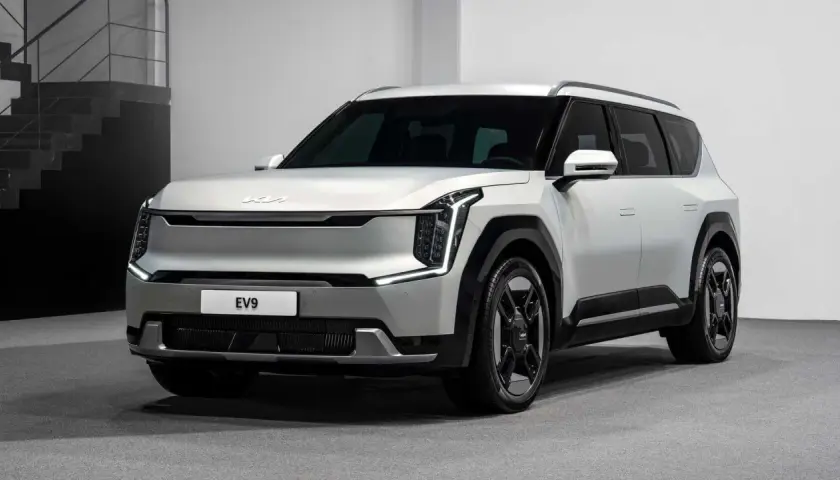Biały, futurystyczny SUV Kia EV9 z charakterystycznymi światłami LED i masywnymi felgami stoi na szarym tle.