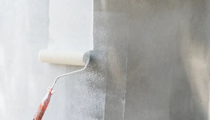 Rodillo aplicando imprimación blanca sobre pared gris. La imprimación prepara la superficie para la pintura.