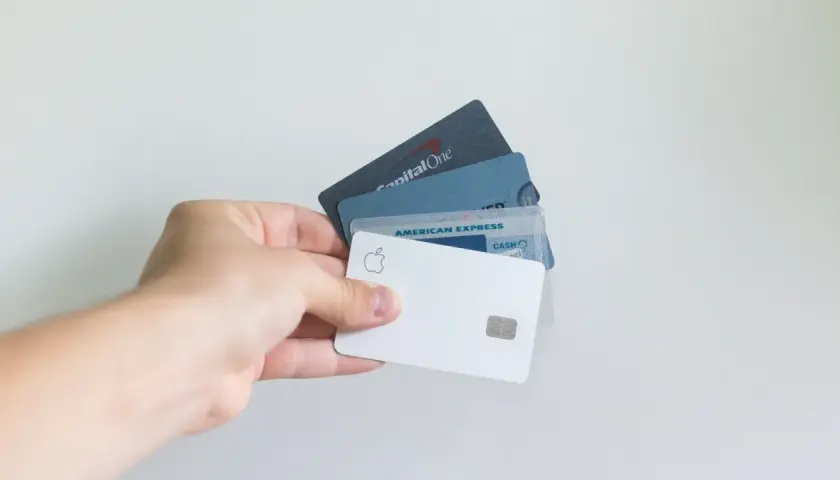 Dłoń trzyma kilka kart, w tym białą kartę Apple i kartę American Express. To jak karta przedpłacona bez konta, wygodna w użyciu.