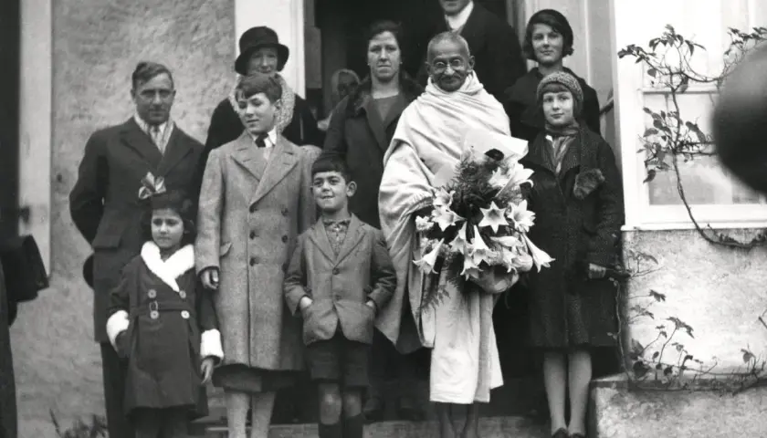 Mahatma Gandhi mit seiner Familie und Freunden, umgeben von Kindern, die Blumen halten.