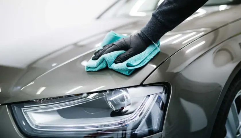 Mano guantata lucida la carrozzeria di un'auto con un panno azzurro. Il dettaglio mostra la cura per il costo lucidatura auto.