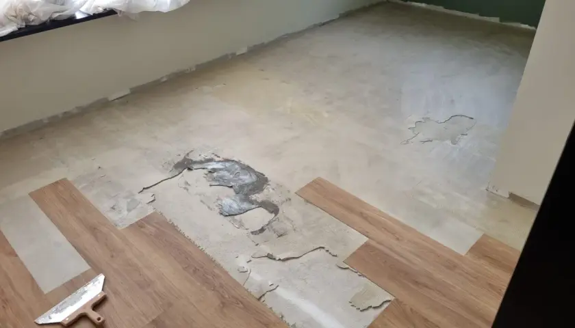 Il pavimento in PVC si solleva in più punti, mostrando il sottofondo danneggiato. Si vedono nuove doghe di legno pronte per la posa.