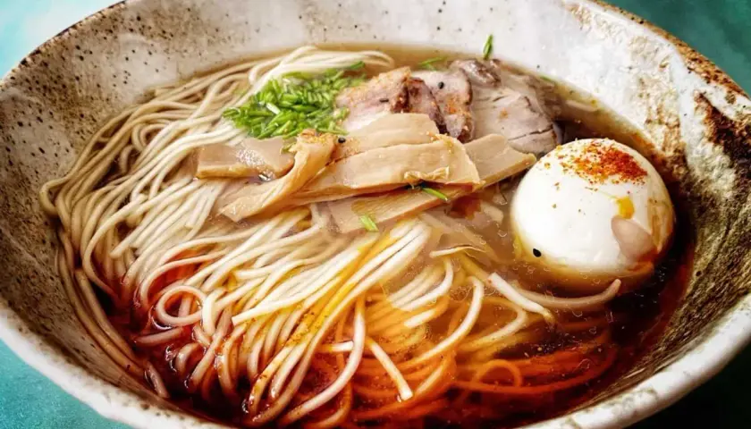Pyszny, domowy ramen z makaronem, plastrami mięsa, bambusem i jajkiem na twardo, posypany szczypiorkiem i papryką.