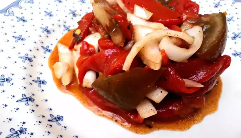 Deliciosa ensalada de pimientos asados con cebolla, bañada en un aderezo rojizo. Un plato lleno de sabor y color.