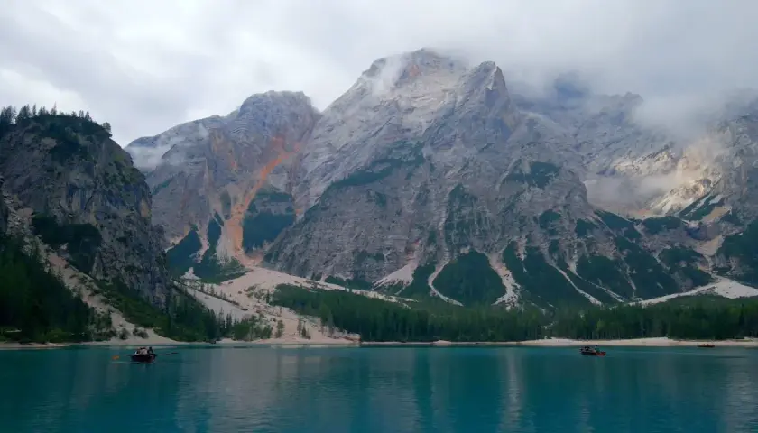 Boote auf einem türkisfarbenen See vor majestätischen Bergen, die an die Alta Via 1 erinnern.