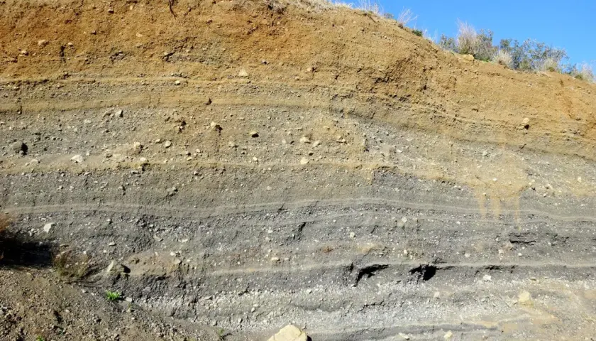 Capas de tierra y grava expuestas en un corte, mostrando la geología del volca de la Crosa.