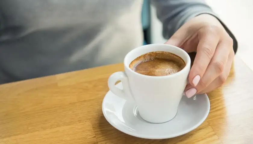 Dłoń sięga po filiżankę kawy, która może wywołać ból głowy po kawie.