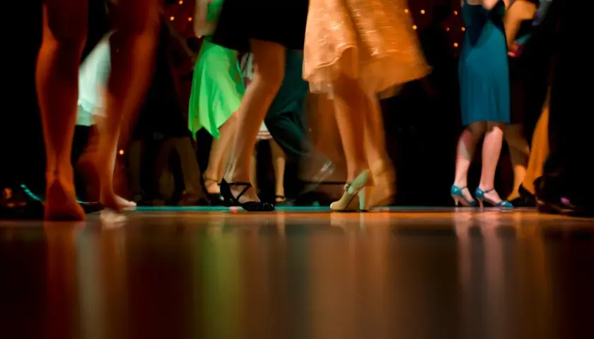 Nogi w ruchu, błyszczące sukienki i eleganckie buty. Wszyscy tańczą, tworząc dynamiczny obraz, jakby to był belgijka taniec.