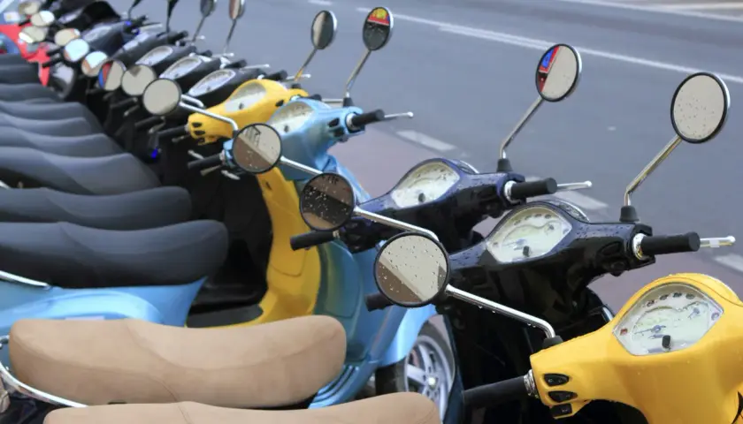 Línea de motos y scooters de colores aparcadas en la calle. Para saber si una moto está libre de cargas, revisa su documentación.