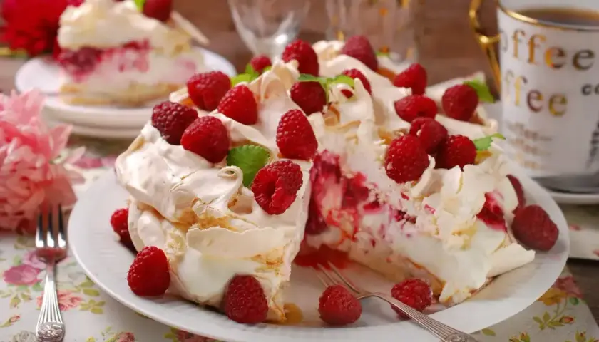 Pyszny tort bezowy z mascarpone i malinami, udekorowany świeżymi owocami i listkami mięty. Idealny na deser.