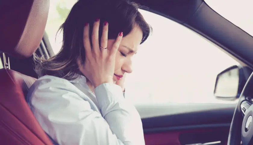Donna in auto si tappa le orecchie per il fastidioso cigolio macchina.