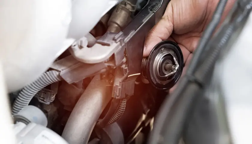 Mano che rimuove la valvola termostatica, forse perché non chiude bene e causa problemi al motore.