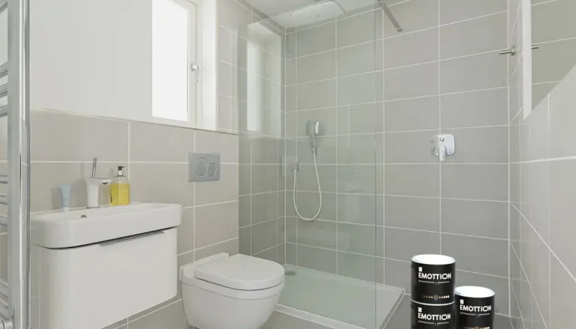Bagno moderno con piastrelle grigie, doccia a filo pavimento e due barattoli di pittura per piastrelle.