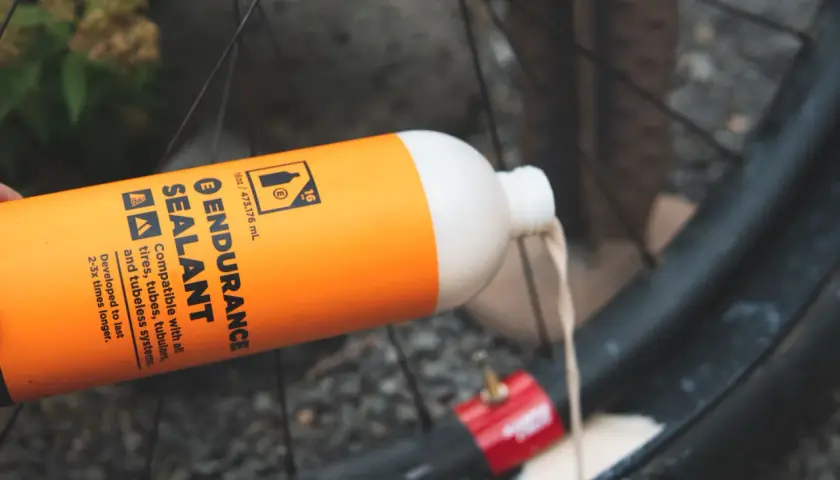 Pouring orange Endurance Sealant into a bike tire. This sealant is designed for longer-lasting protection compared to regular options.