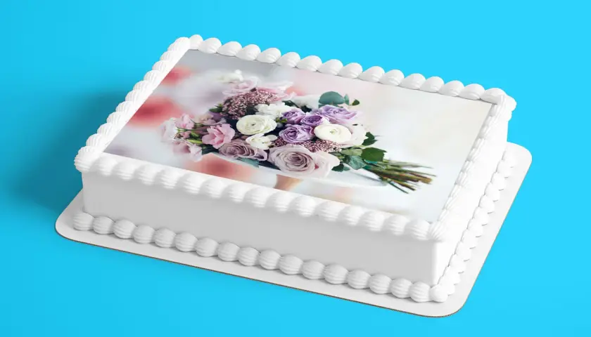 Gâteau blanc décoré d'un bouquet de fleurs roses et violettes sur une feuille azyme. Parfait pour une recette festive.
