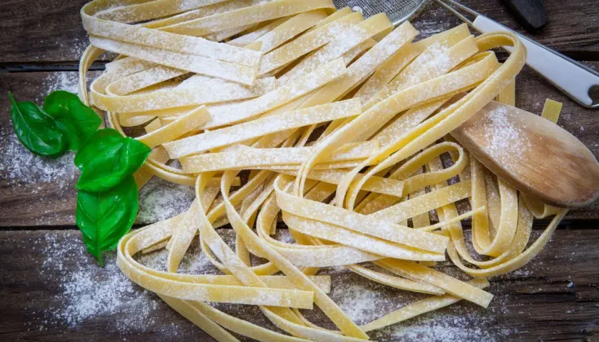 Świeży makaron tagliatelle, posypany mąką, z listkami bazylii. Idealny jako alternatywa, czym zastąpić makaron pszenny.