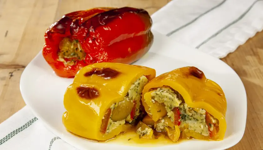 Peperoni ripieni senza carne, un piatto colorato e saporito. Un peperone rosso intero e uno giallo tagliato a metà, entrambi farciti con un ripieno gustoso.