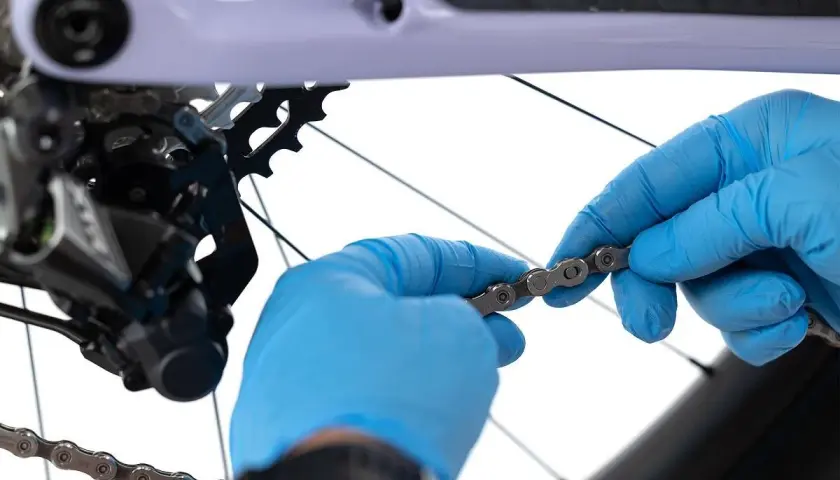 Ręce w niebieskich rękawiczkach sprawdzają kierunek łańcucha rowerowego przed jego montażem.