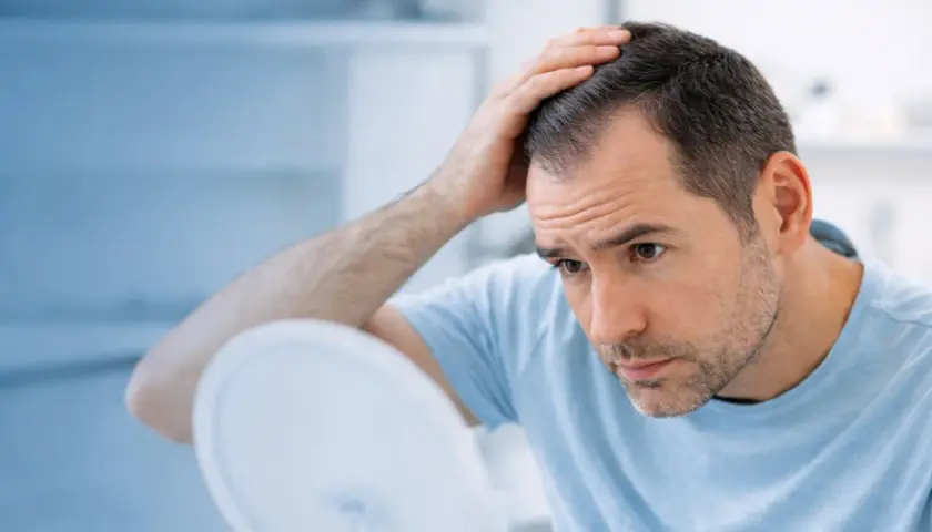 Hombre preocupado se toca la cabeza, observando las entradas en el pelo en el espejo.
