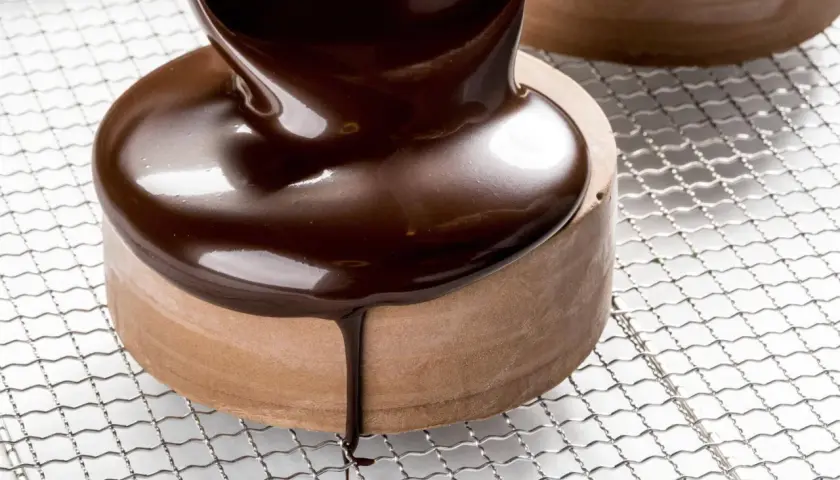 Un glaçage chocolat brillant et onctueux recouvre un petit gâteau rond, coulant sur les côtés.