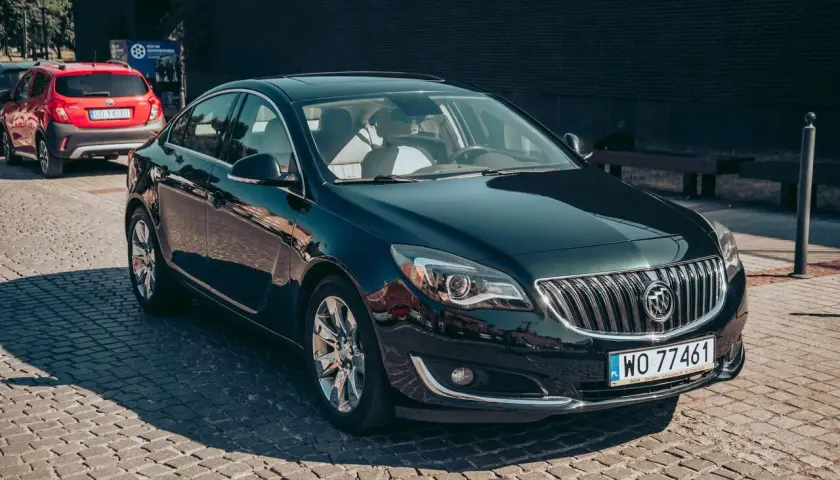 Elegancki, ciemnozielony Buick Regal z chromowanymi felgami stoi na brukowanej ulicy.