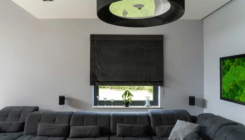 Elegancka roleta rzymska do salonu, wykonana z ciemnego materiału, tworzy przytulną atmosferę.