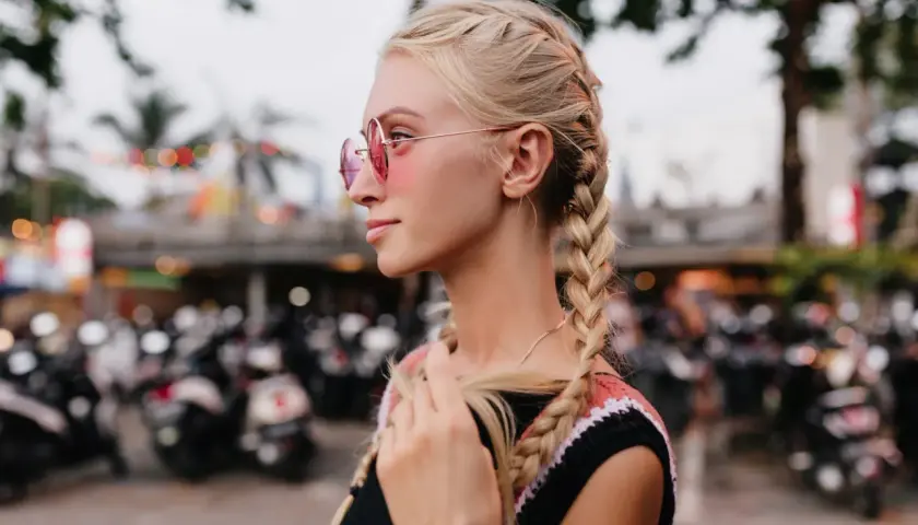 Blondynka w okularach przeciwsłonecznych z dwoma warkoczami na tle skuterów.