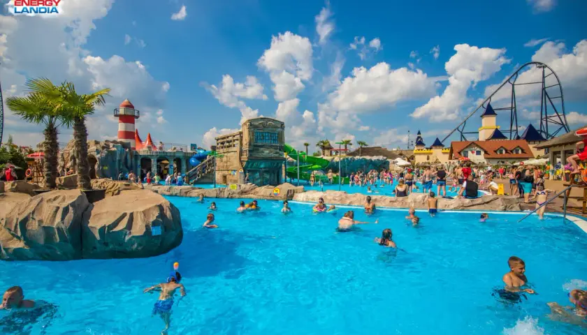 Energylandia strefa wodna tętni życiem. Ludzie kąpią się w basenie, bawią na zjeżdżalniach, a w tle widać rollercoaster.