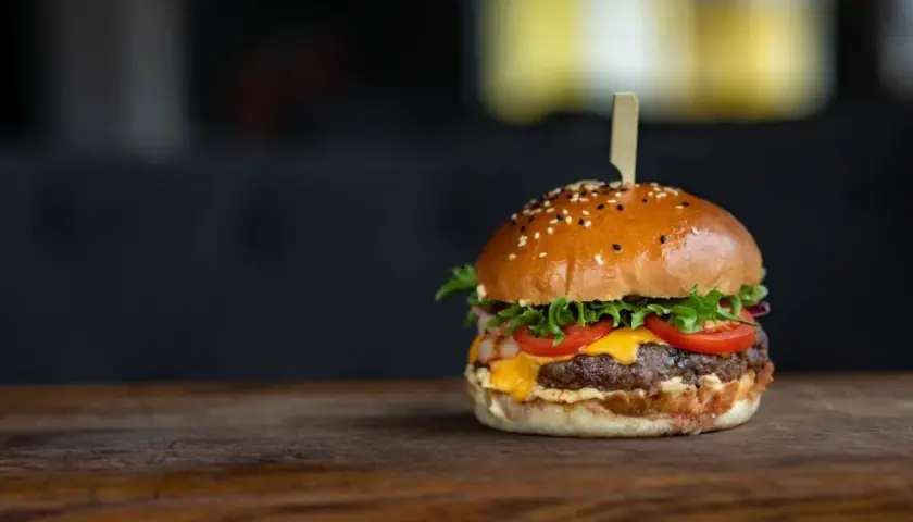 Apetyczny hamburger z serem, pomidorami i sałatą na drewnianym blacie.