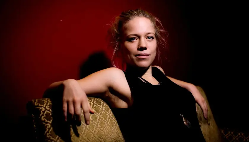 Olivia Bergdahl sitter avslappnat i en soffa, med en mörk bakgrund och en blick som fångar.
