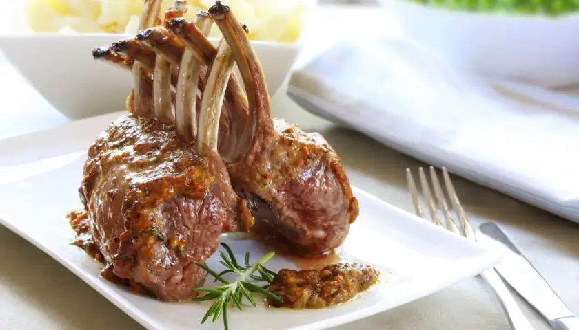 Un délicieux carré d'agneau rôti, nappé d'une sauce savoureuse, est servi avec une branche de romarin.