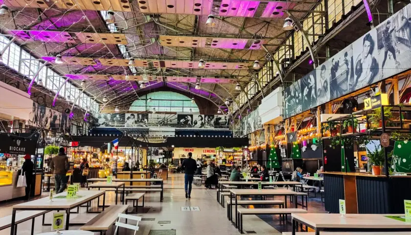Wegańskie restauracje Warszawa w hali targowej z neonami i czarno-białymi zdjęciami na ścianach. Wiele stolików i ław, ludzie jedzą i spacerują.