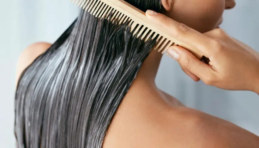 Persona peina su mascarilla en pelo seco antes de lavar, preparándolo para un tratamiento intensivo.