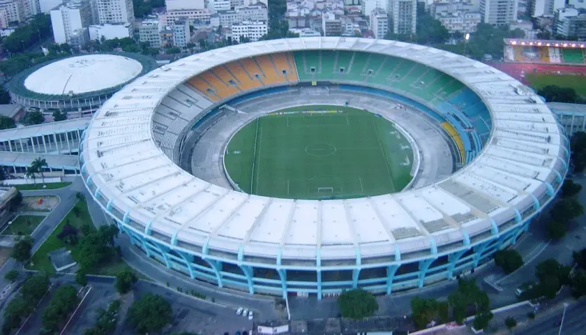 Widok z lotu ptaka na stadion Maracanã z zieloną murawą i kolorowymi trybunami, otoczony miejską zabudową.