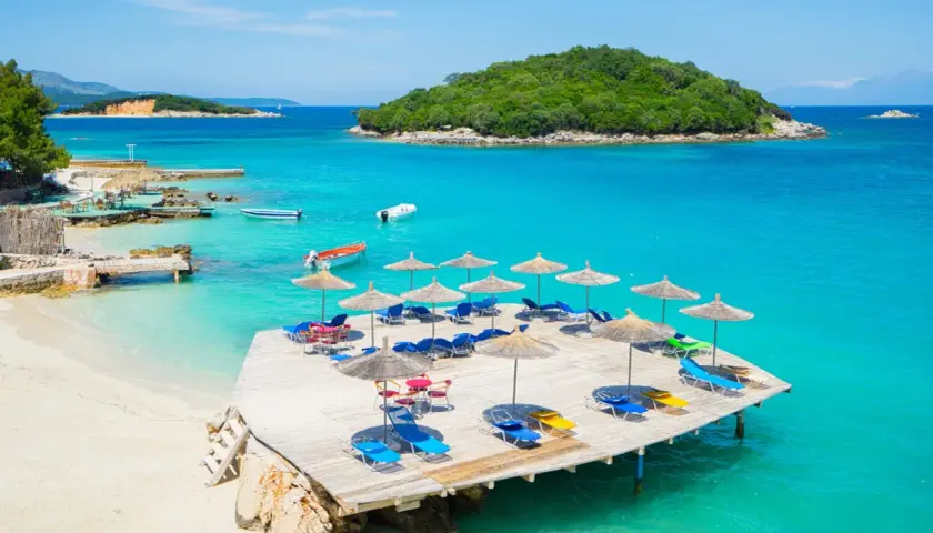 Rajskie albania plaże z turkusową wodą, drewnianym molo i leżakami pod parasolami.