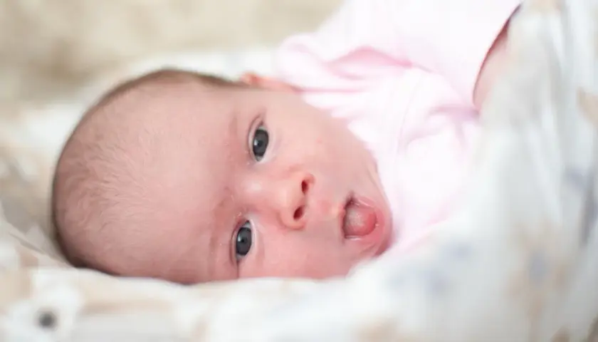 Neonato con lingua bianca, vestito di rosa, guarda incuriosito.