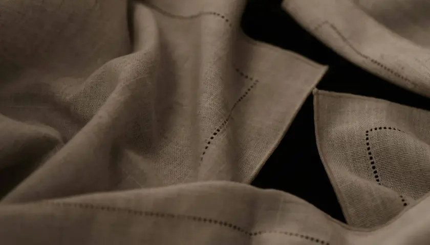 Draped linen fabric, perfect for breathable summer pants, features delicate dotted stitching along its edges.