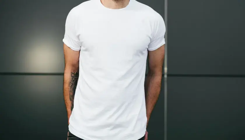 Mann mit Bart trägt weißes T-Shirt und Jeans, Hände in den Taschen.