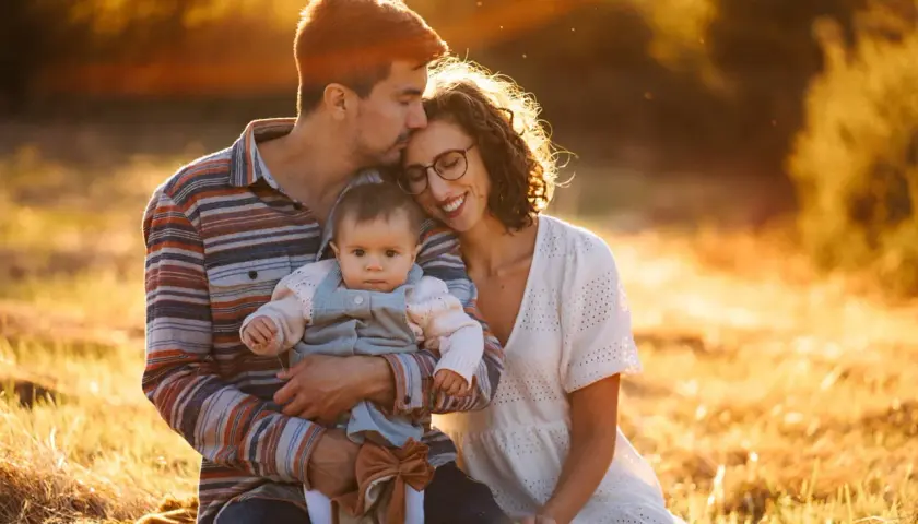 Piękne zdjecia rodzinne w złotym świetle zachodzącego słońca. Tata obejmuje córeczkę, mama wtula się w tatę.