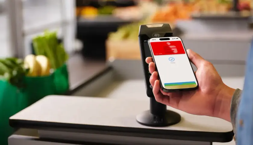 Einkaufen leicht gemacht: So funktioniert Apple Pay. Ein iPhone wird zum Bezahlen an ein Terminal gehalten, im Hintergrund sind Lebensmittel zu sehen.