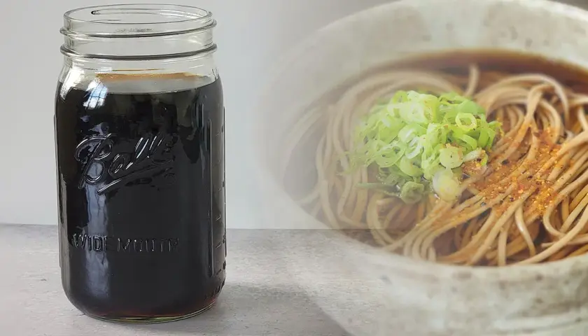 A jar of dark soba dipping sauce sits next to a bowl of soba noodles with green onions. Perfect for your soba dipping sauce recipe.